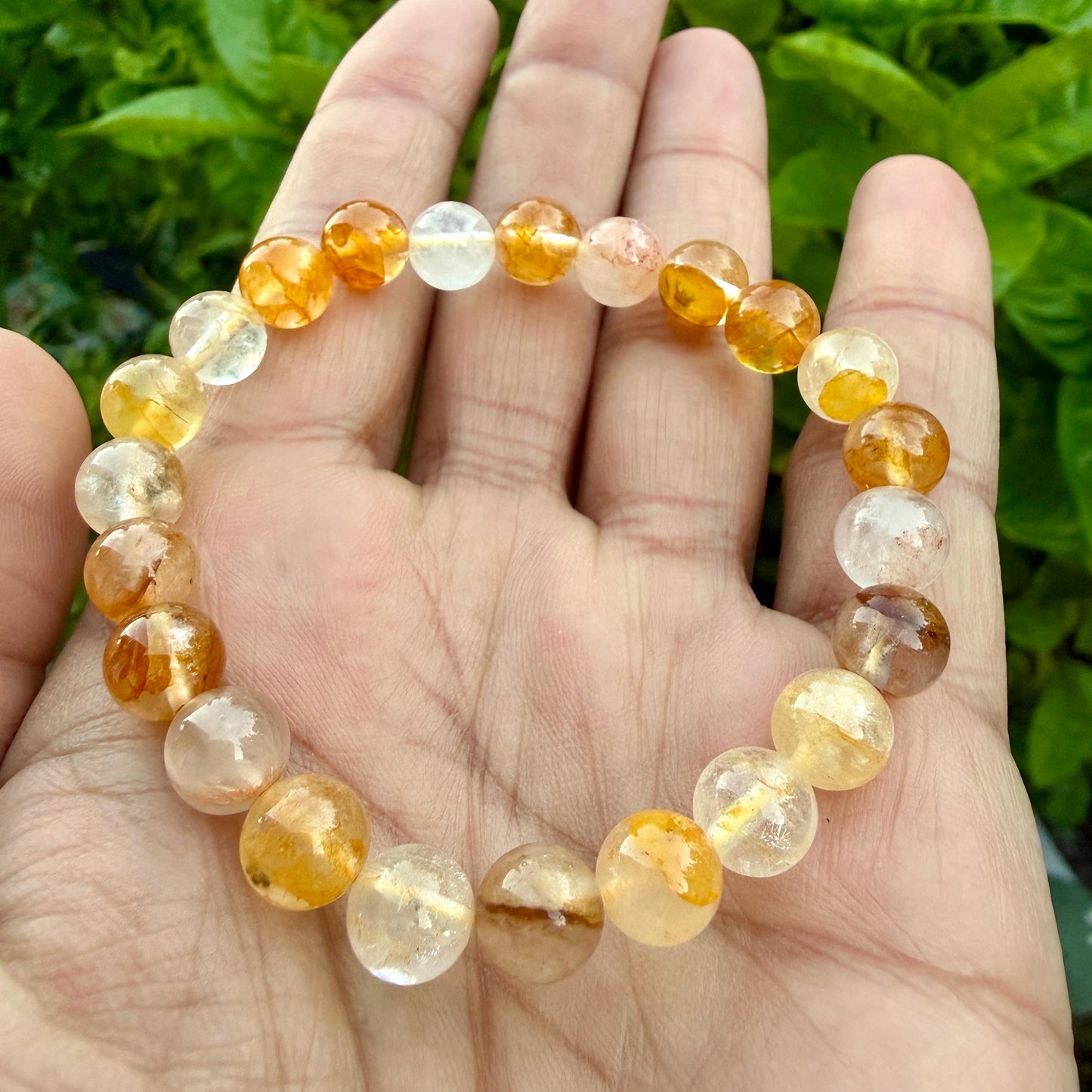 May include: A stretch bracelet composed of round, polished beads in varying shades of translucent yellow, orange, and clear quartz. The beads exhibit natural internal inclusions and color gradients, arranged in a circular pattern on an elastic cord.
