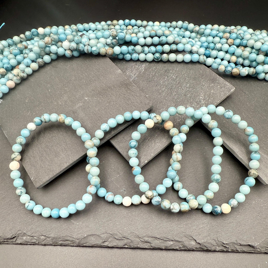 Pale sky-blue larimar bead bracelet strands resting on dark slate