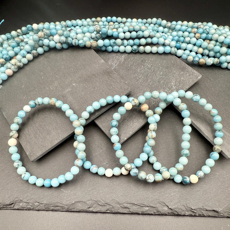 Pale sky-blue larimar bead bracelet strands resting on dark slate