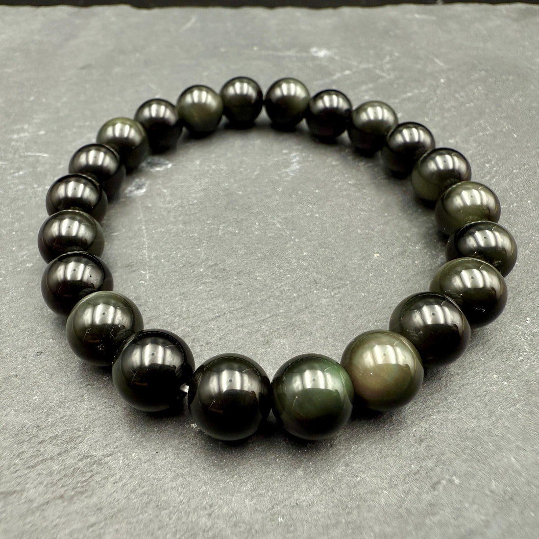 Polished black obsidian beaded bracelet with a subtle rainbow sheen on grey slate