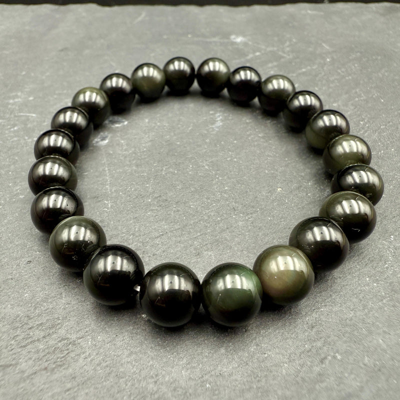 Polished black obsidian beaded bracelet with a subtle rainbow sheen on grey slate