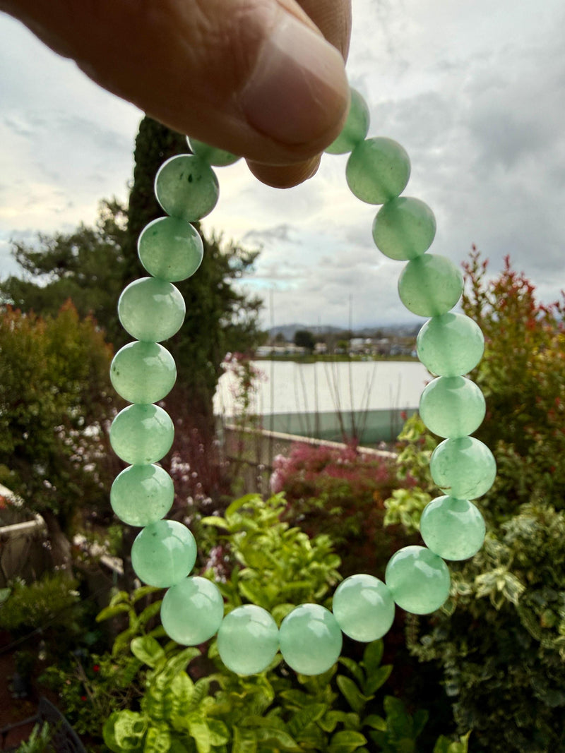 Pale green aventurine beaded bracelet held up to soft daylight against a garden background