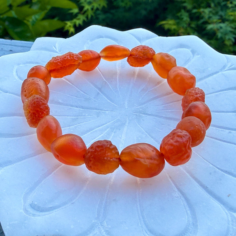 Warm orange carnelian beaded bracelet resting on a white lotus dish with greenery behind