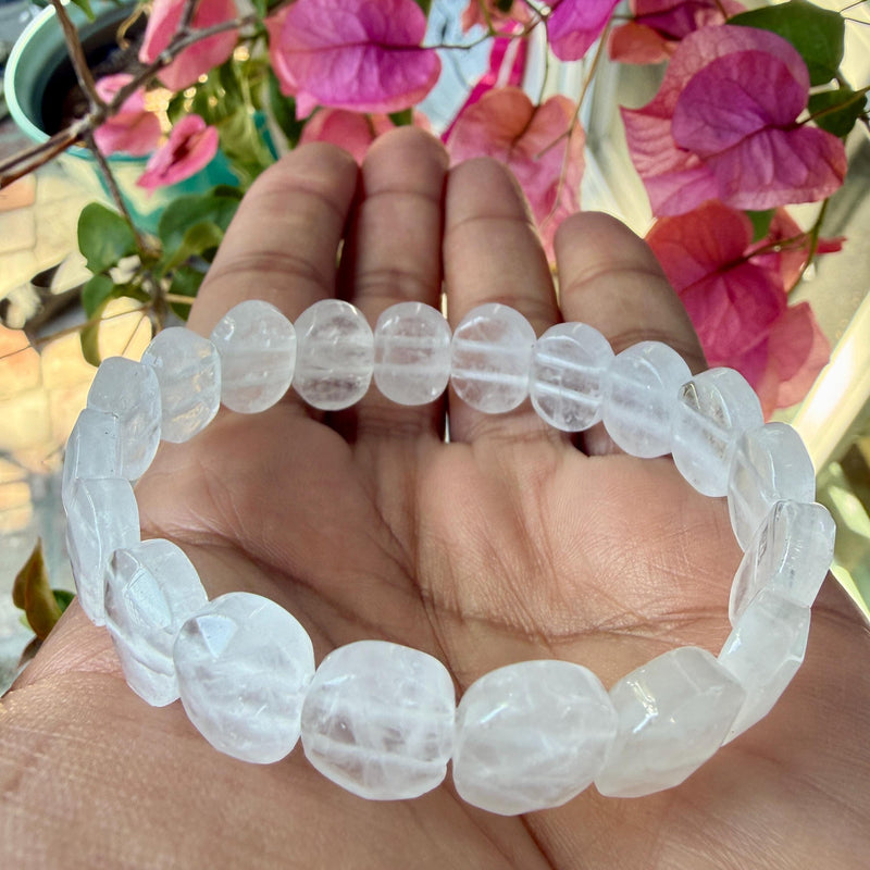 Clear quartz faceted bead bracelet resting in an open palm with pink flowers behind