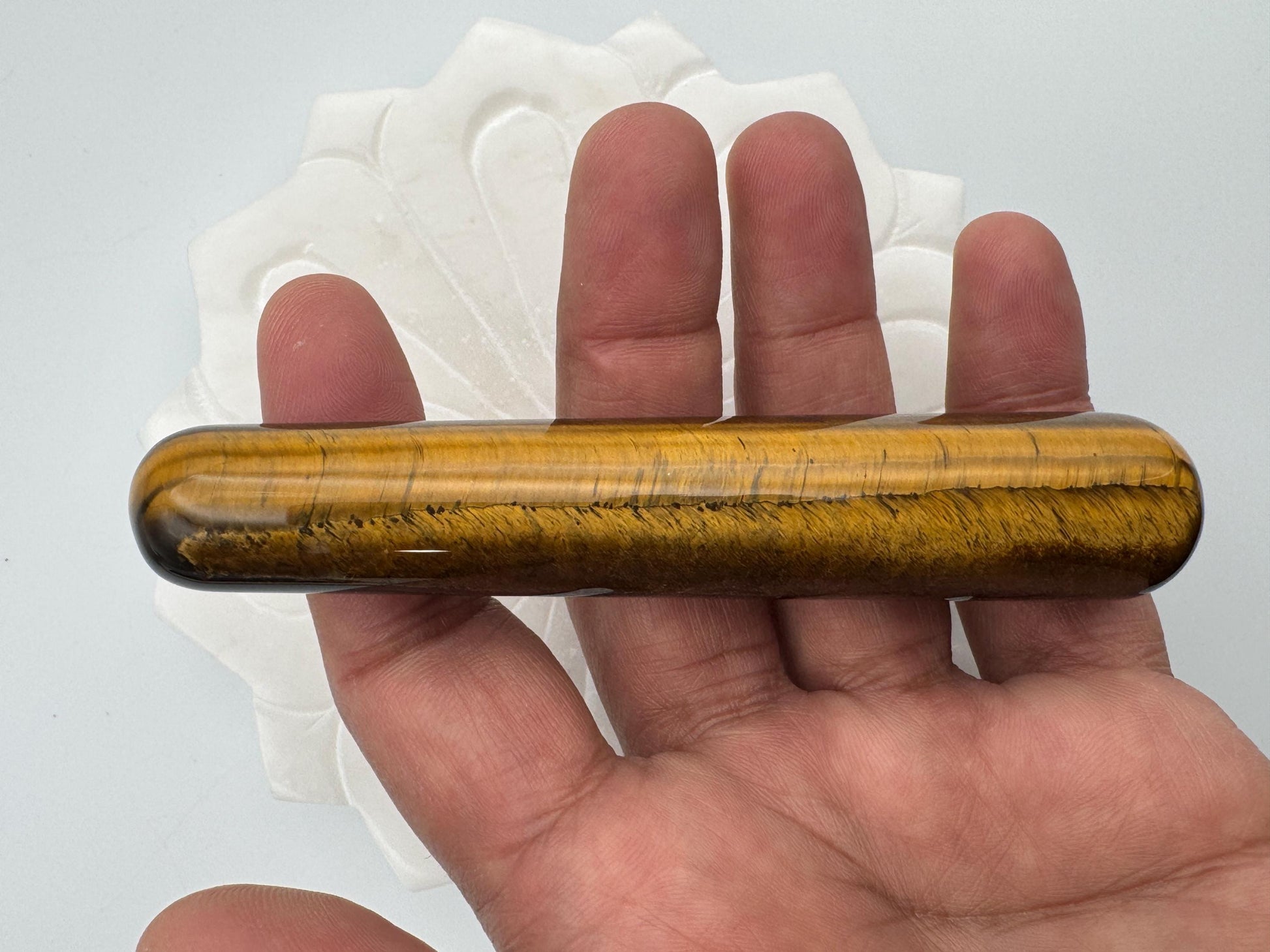 Hand holding a tiger's eye stone against a white background