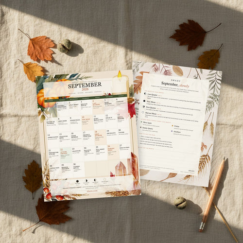 Both printed pages of the September 2026 Energy Calendar laid on linen with dried autumn leaves