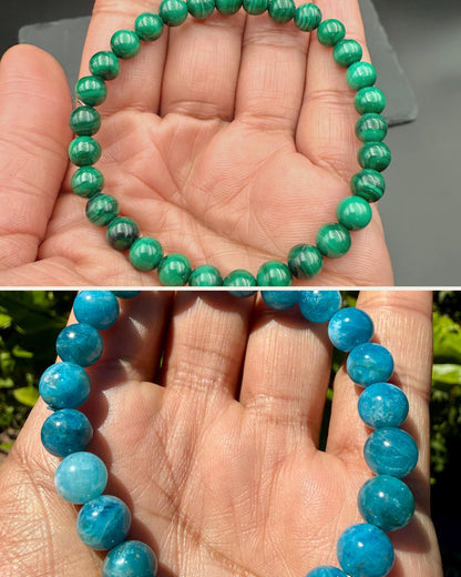 Malachite bracelet held in a palm above a blue apatite bracelet held in a palm outdoors