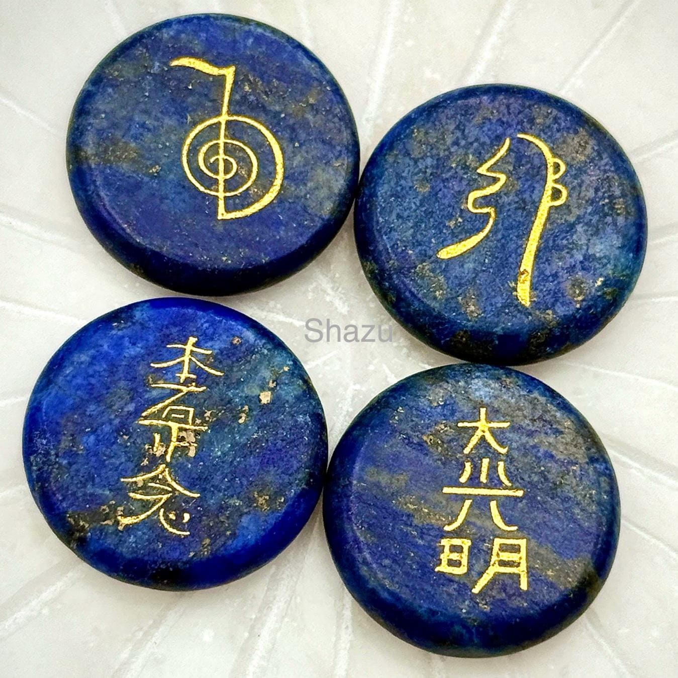 May include: Four round, deep blue lapis lazuli stones with gold-colored symbols and characters. The stones have a polished surface and varying patterns. The image includes the word "Shazu".