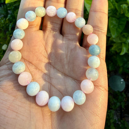 May include: A stretch bracelet composed of smooth, round beads in alternating shades of pale pink, soft blue, and creamy off-white. The beads are strung together in a circular pattern, creating a continuous loop of pastel-colored stones.