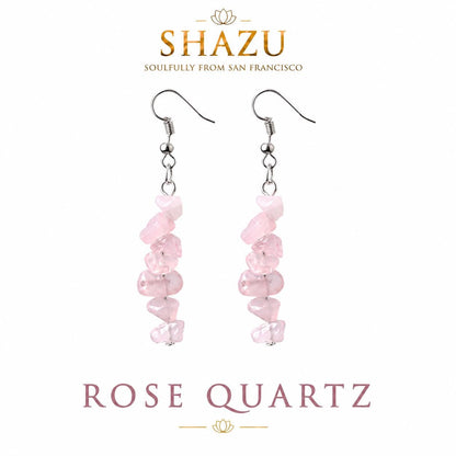 May include: Dangle earrings featuring irregular, tumbled light pink rose quartz chips strung on silver-toned metal hooks. The text SHAZU SOULFULLY FROM SAN FRANCISCO and ROSE QUARTZ appears above and below the earrings on a white background.