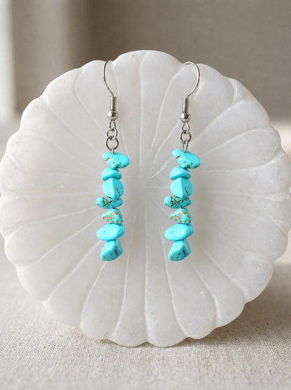 May include: A pair of dangle earrings featuring vertical strands of irregular, bright turquoise blue stone chips with brown matrix veining. The stones are suspended from silver-toned metal fishhook ear wires, creating a linear drop design.