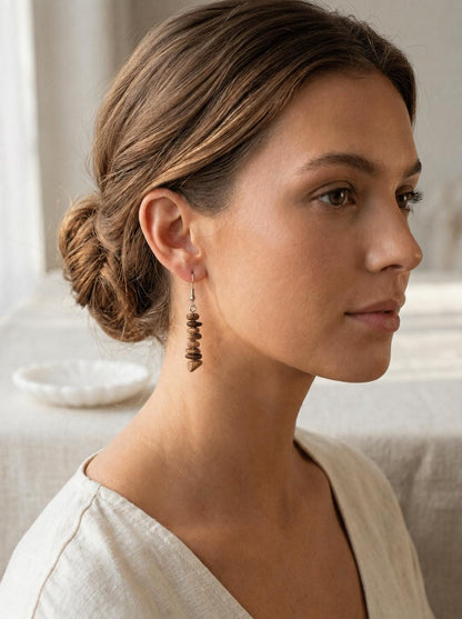 May include: A drop earring featuring a vertical stack of small, polished, brown and tan stone beads suspended from a silver-toned metal hook. The beads are irregular in shape and vary in shades of earthy brown, creating a textured, linear design.