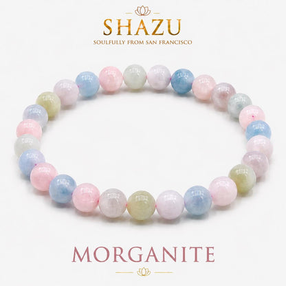 May include: A beaded bracelet featuring smooth, round, polished gemstones in pastel shades of pink, blue, and pale yellow. The bracelet is arranged in a circular shape. Above the bracelet, the text reads SHAZU SOULFULLY FROM SAN FRANCISCO, and below it, the text reads MORGANITE.