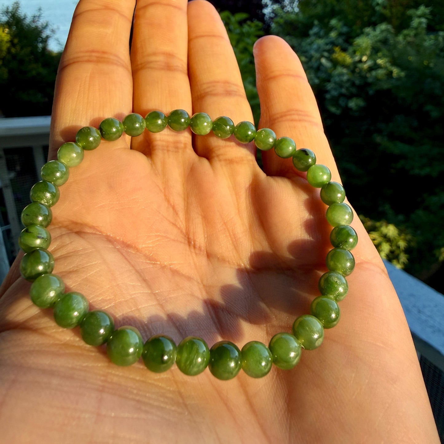 May include: A circular bracelet composed of small, smooth, spherical beads in varying shades of translucent forest green. The beads are strung together in a continuous loop, displaying natural color variations and a polished, reflective surface finish.