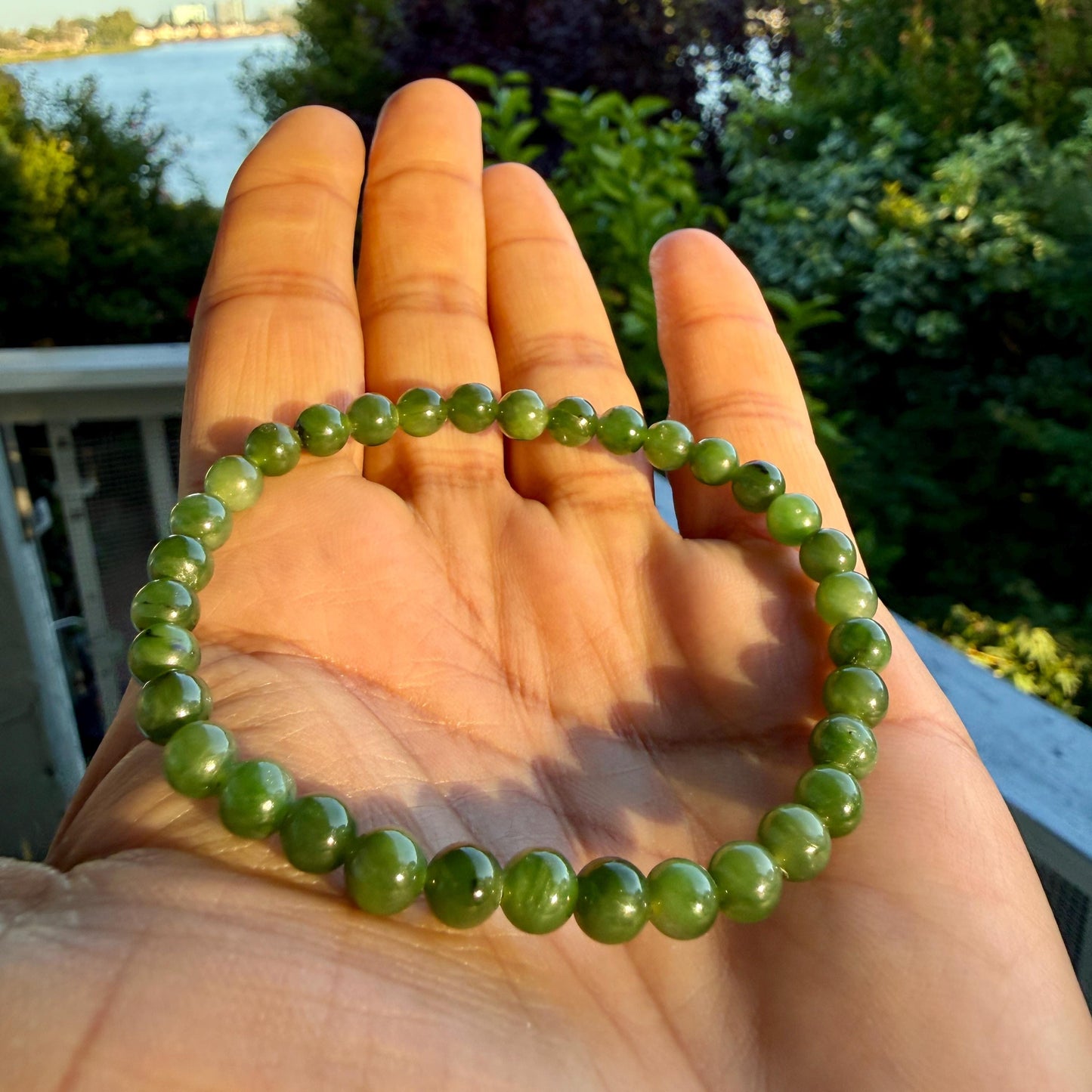May include: A circular bracelet composed of small, smooth, spherical green beads. The beads exhibit varying shades of translucent and opaque olive green, strung together in a continuous loop to form a simple, uniform band of polished stone.