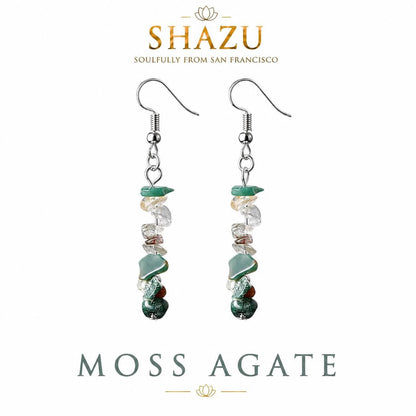 May include: A pair of drop earrings featuring silver-toned hooks and a vertical arrangement of tumbled moss agate and clear quartz stone chips. The text SHAZU SOULFULLY FROM SAN FRANCISCO and MOSS AGATE is visible above and below the earrings.