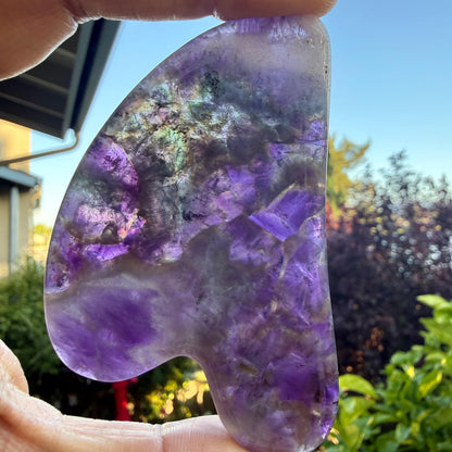 May include: A polished, heart-shaped amethyst stone featuring deep purple and translucent white crystalline patterns. The surface displays natural mineral inclusions and variations in color density, with smooth, rounded edges throughout the piece.