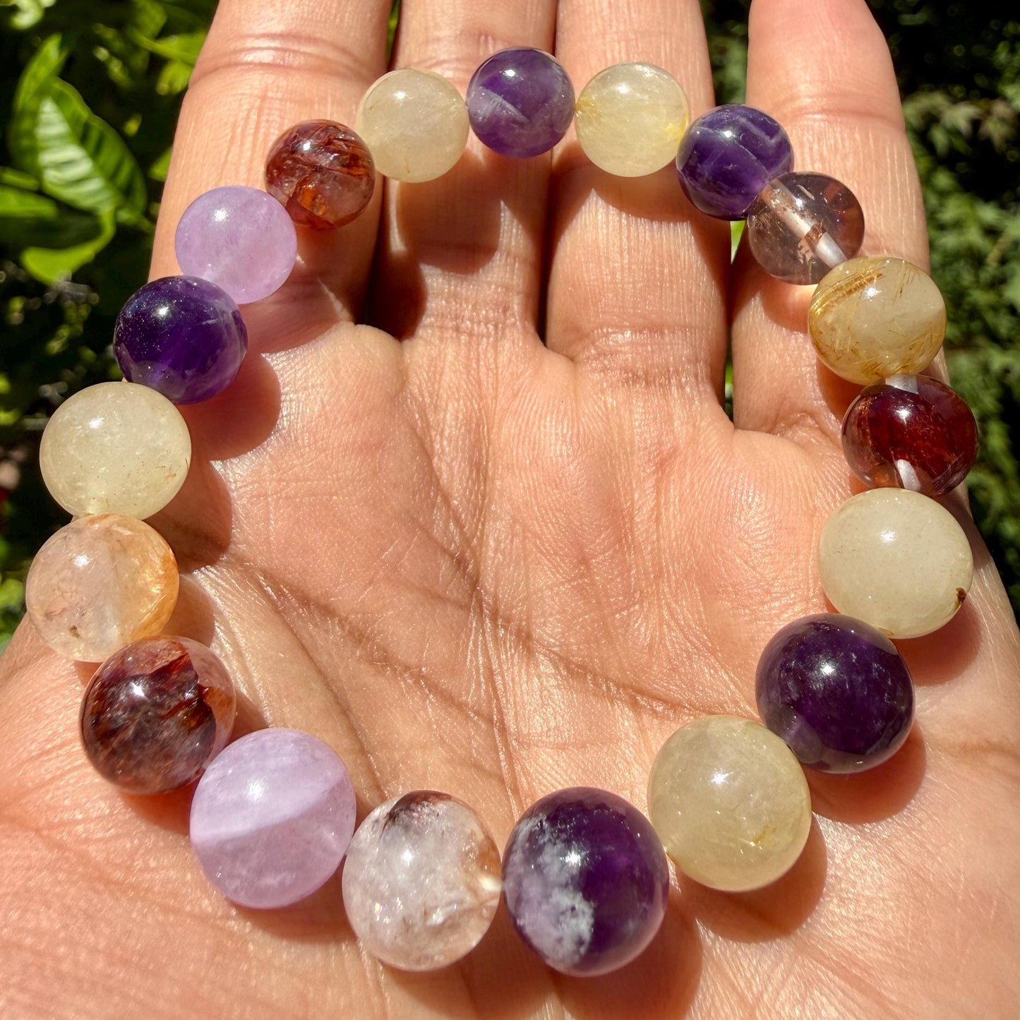 May include: A stretch bracelet composed of round, polished gemstone beads in various colors including deep purple amethyst, translucent yellow citrine, and reddish-brown rutilated quartz, arranged in a repeating pattern on an elastic cord.