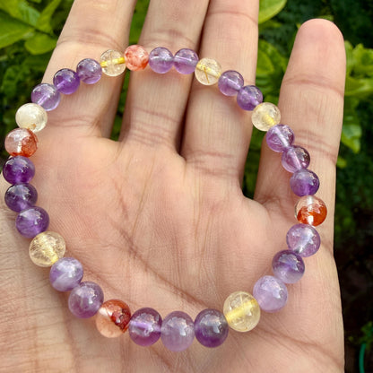 May include: A beaded bracelet featuring a circular arrangement of polished spherical gemstones in shades of purple, translucent yellow, and orange-red. The beads are strung together on an elastic cord, creating a continuous loop of smooth, multi-colored stones.