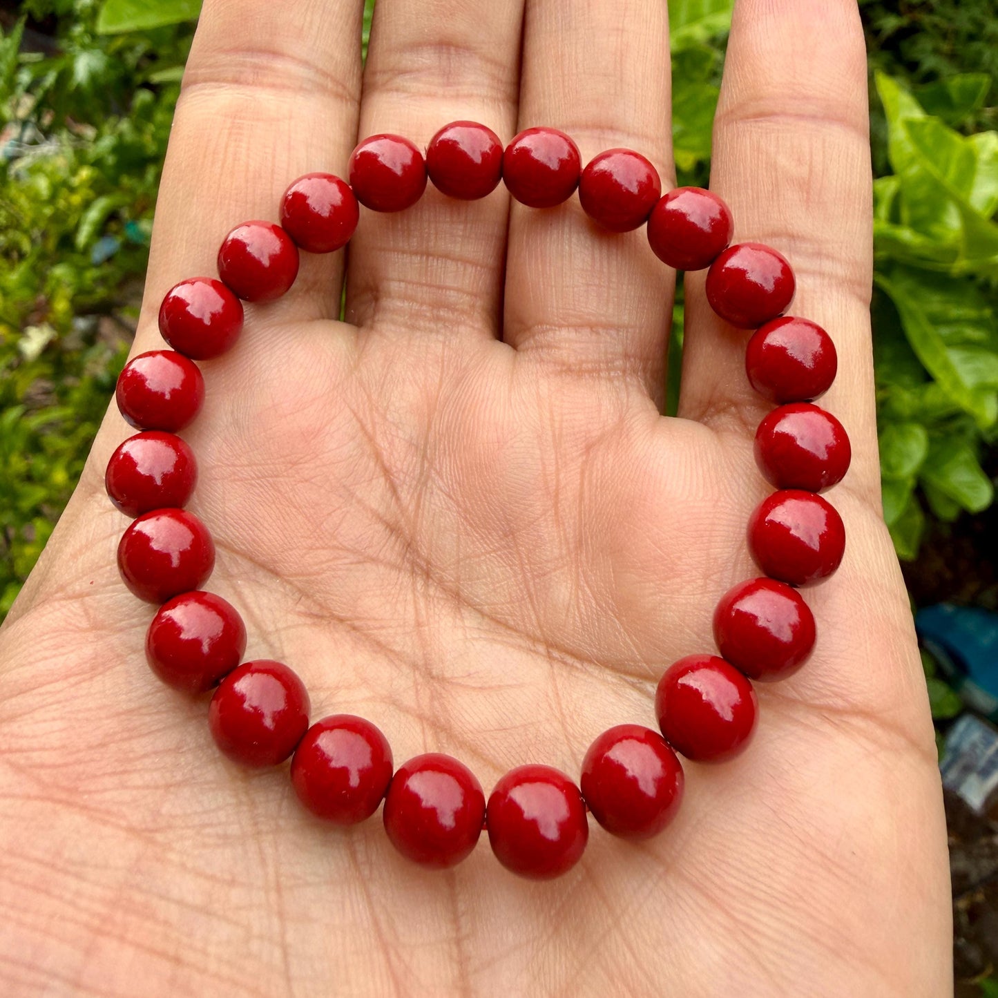 May include: A circular stretch bracelet composed of twenty-two smooth, glossy, solid red spherical beads of uniform size. The beads are strung together in a continuous loop, creating a simple, rounded design with a vibrant, consistent red color.
