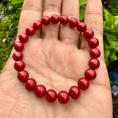 May include: A circular stretch bracelet composed of twenty-two smooth, glossy, solid red spherical beads of uniform size. The beads are strung together in a continuous loop, creating a simple, rounded design with a vibrant, consistent red color.