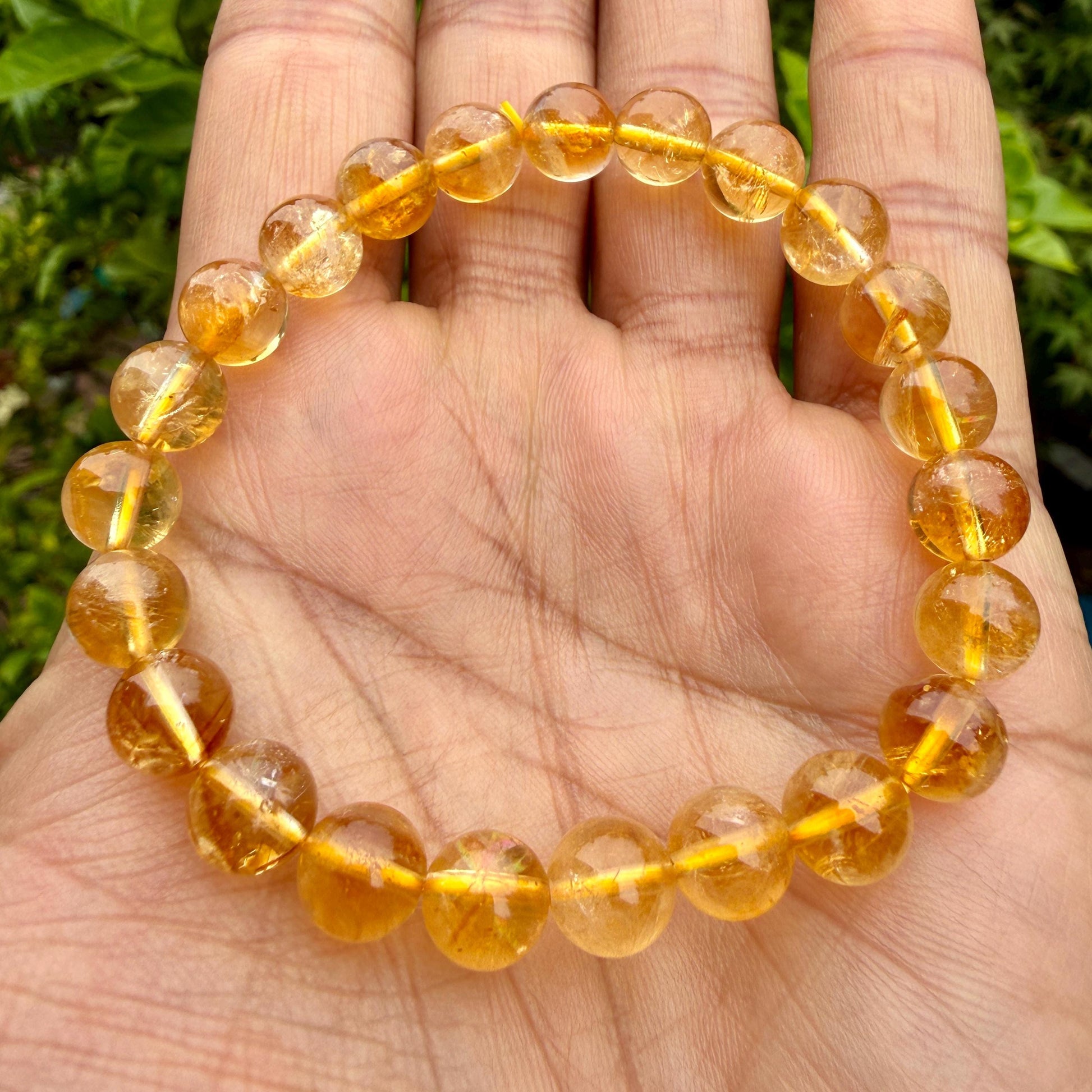 May include: A circular bracelet composed of translucent, golden-yellow citrine beads strung on a thin, bright yellow elastic cord. The beads are polished to a smooth, reflective finish, showcasing natural internal variations and warm amber tones.