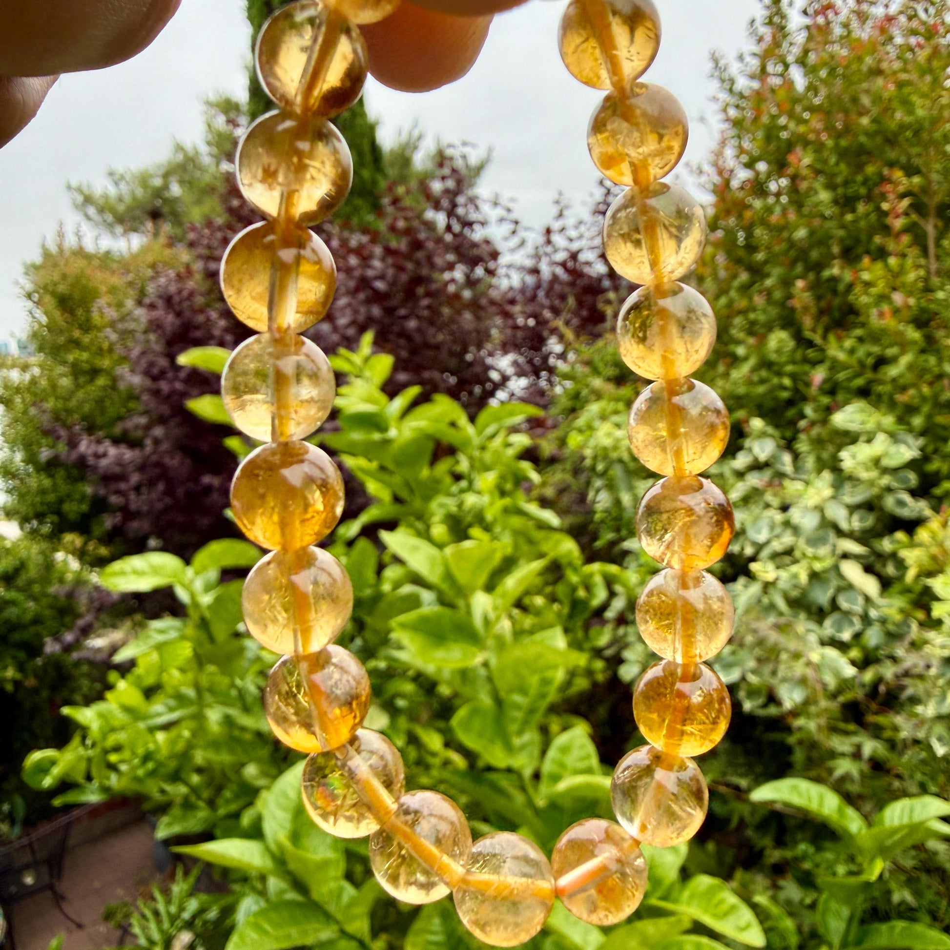 May include: A beaded bracelet featuring translucent, round, golden-yellow citrine gemstones strung together. Each bead displays a smooth, polished surface with natural internal inclusions and variations in color intensity throughout the strand.
