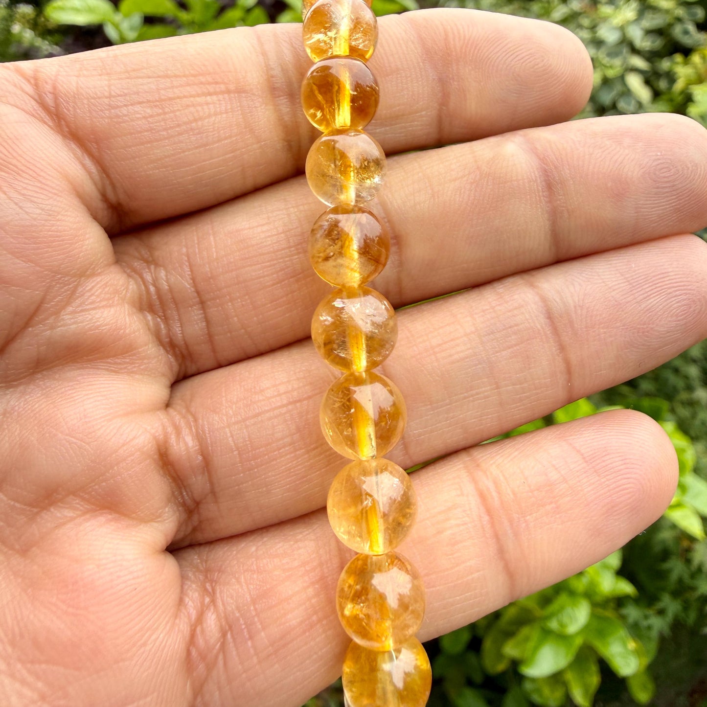 May include: A strand of translucent, round, golden-yellow citrine beads strung together. Each bead displays a smooth, polished surface with natural internal variations and clarity, reflecting light through the warm, honey-colored gemstone spheres.