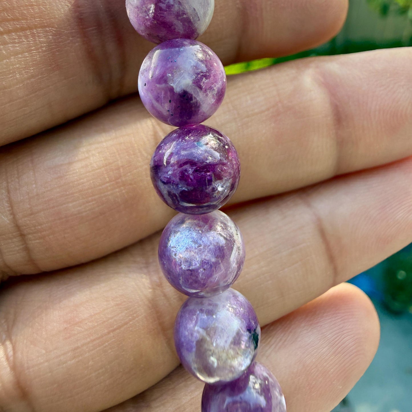 May include: A strand of spherical beads featuring a marbled pattern of deep purple, violet, and white tones. Each bead has a smooth, polished surface with natural variations in color intensity and opacity, creating a unique look for each individual piece.