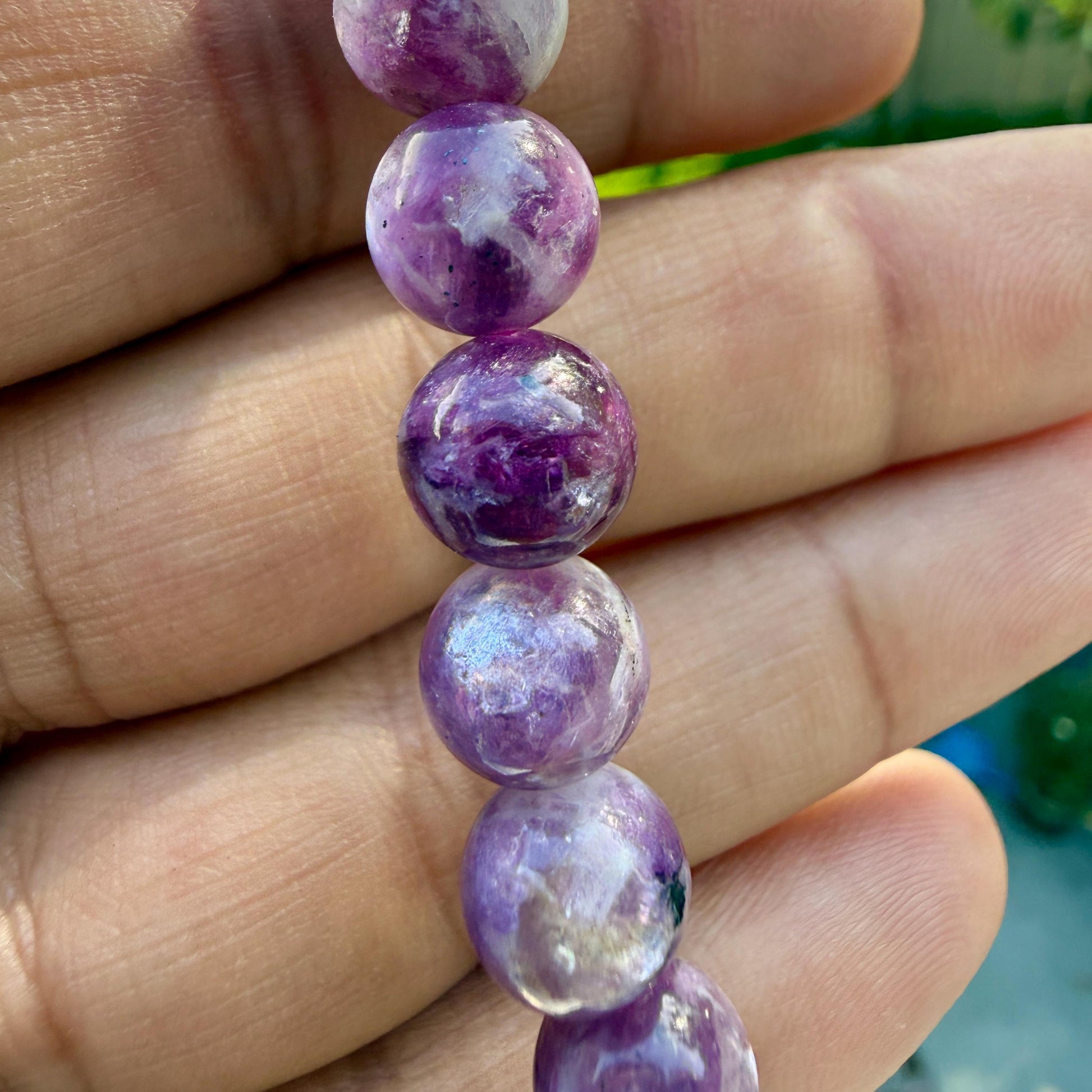 May include: A strand of spherical beads featuring a marbled pattern of deep purple, violet, and white tones. Each bead has a smooth, polished surface with natural variations in color intensity and opacity, creating a unique look for each individual piece.