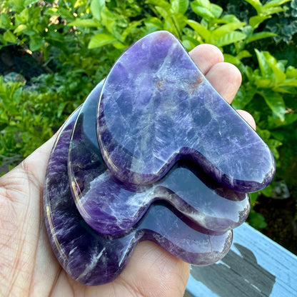May include: Three polished amethyst stones shaped like hearts, stacked in a cascading arrangement. The stones feature deep purple hues with natural white crystalline inclusions and a smooth, glossy surface texture throughout the pieces.