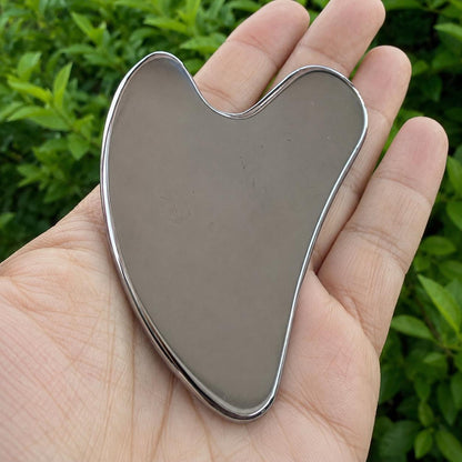 May include: A heart-shaped gua sha tool with a smooth, reflective metallic surface. The object features a curved, ergonomic design with rounded edges and a polished finish, showcasing a solid, uniform grey color throughout its entire structure.