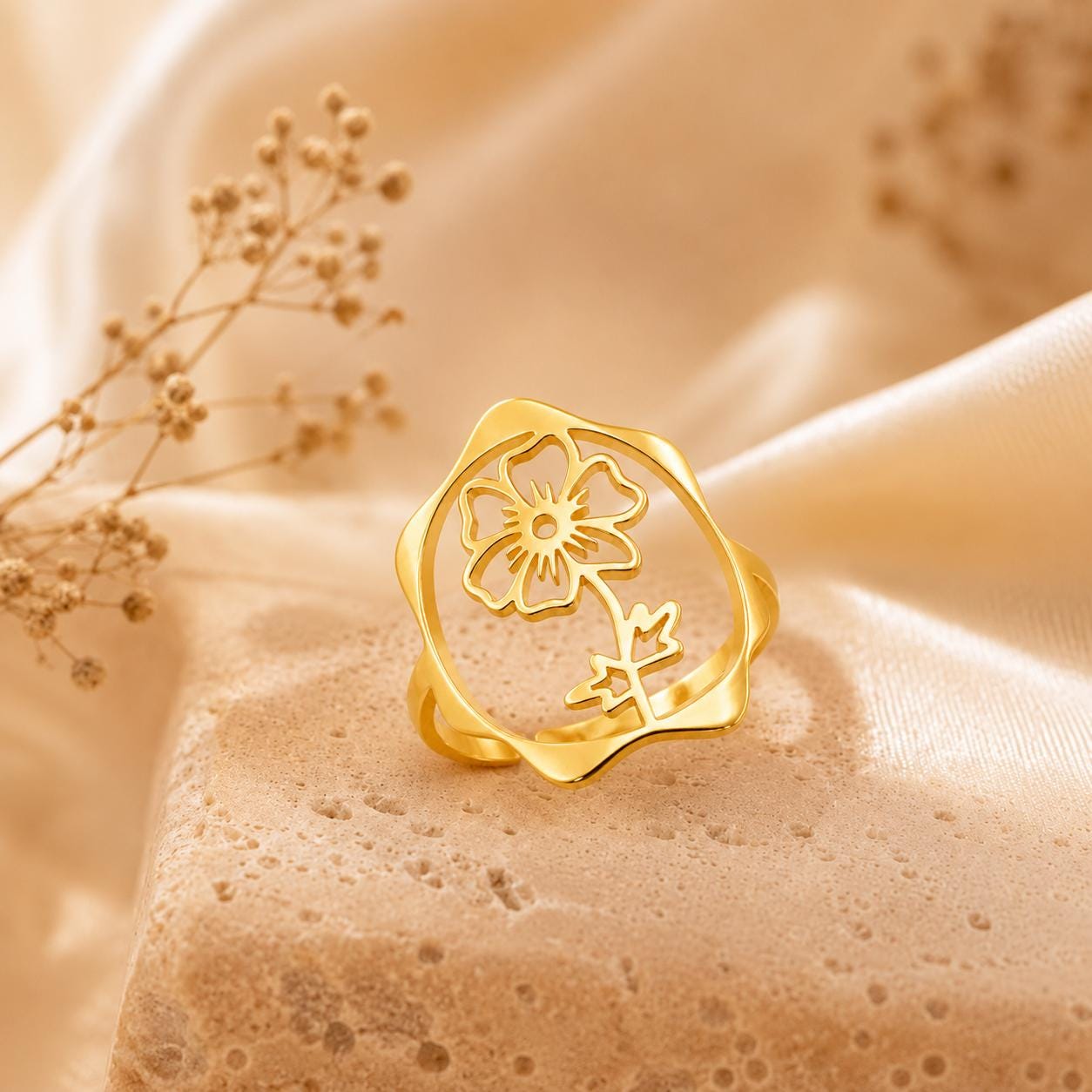 May include: A gold-toned ring featuring an openwork circular design with a central cutout of a five-petaled flower and a stem with leaves. The ring has a smooth, polished finish and a slightly irregular, organic-shaped outer band edge.