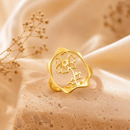 May include: A gold-toned ring featuring an openwork circular design with a central cutout of a five-petaled flower and a stem with leaves. The ring has a smooth, polished finish and a slightly irregular, organic-shaped outer band edge.
