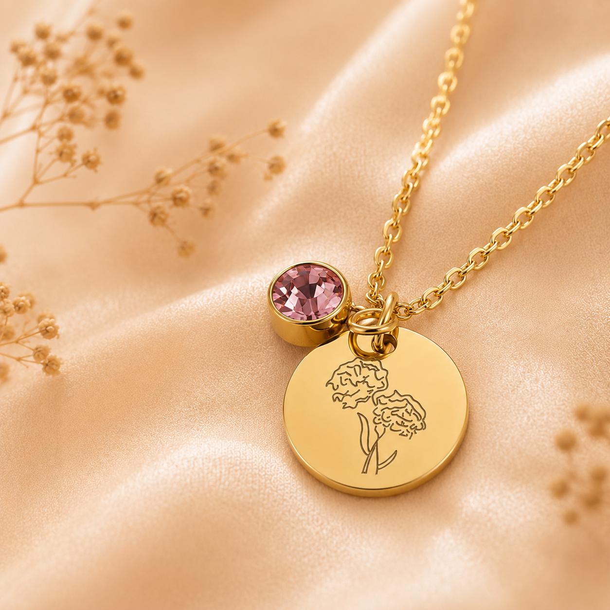 May include: A gold-toned necklace featuring a circular pendant engraved with a line-art floral design and a small, round, faceted pink crystal charm attached to the same link, suspended from a delicate gold-toned metal chain.