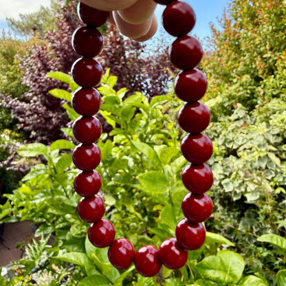 May include: A necklace composed of smooth, round, deep red beads strung together in a continuous loop. The beads have a glossy, reflective finish and are uniform in size, creating a simple, circular strand that hangs vertically in the frame.