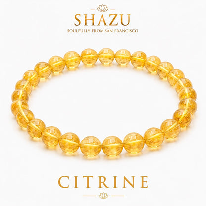 May include: A circular bracelet composed of translucent, golden-yellow citrine beads. Above the bracelet, the text reads SHAZU SOULFULLY FROM SAN FRANCISCO. Below the bracelet, the text reads CITRINE. The beads are uniform in size and shape.