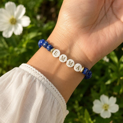 May include: A beaded bracelet featuring deep blue lapis lazuli stones and four white circular beads with the gold-colored letters E, M, M, and A printed on them. The bracelet includes small gold-colored spacers between the beads.