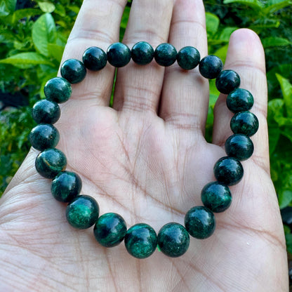 May include: A stretch bracelet composed of round, polished dark green beads with subtle black inclusions. The beads are uniform in size and strung together in a circular loop, displaying a smooth, glossy texture and deep forest green color tones.