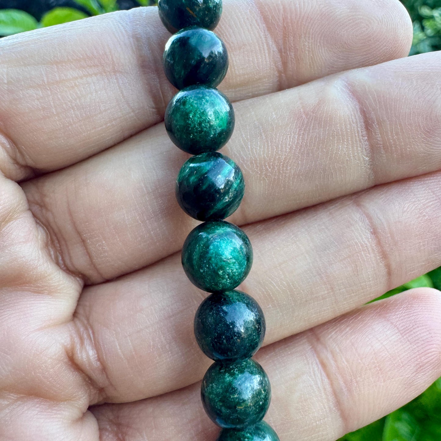 May include: A strand of spherical beads featuring a deep forest green color with swirling patterns of dark black and lighter emerald green tones. The beads have a smooth, polished finish and are arranged in a vertical line, showcasing variations in color.