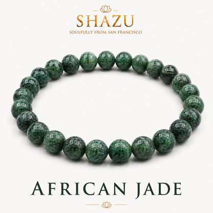 May include: A beaded bracelet made of round, polished African jade stones in shades of deep forest green with dark mottled patterns. The text SHAZU SOULFULLY FROM SAN FRANCISCO and AFRICAN JADE is printed above and below the bracelet.