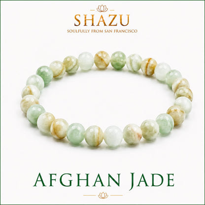 May include: A beaded bracelet made of smooth, round Afghan jade stones in varying shades of translucent pale green, white, and light brown. The text SHAZU SOULFULLY FROM SAN FRANCISCO and AFGHAN JADE is printed in dark green and gold lettering.