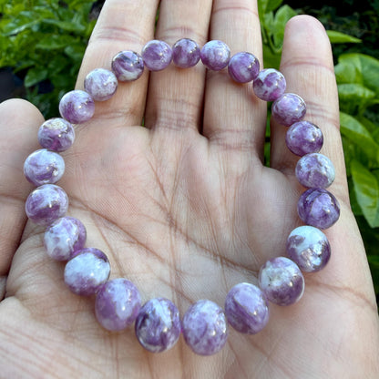 May include: A stretch bracelet composed of round, polished beads in varying shades of purple and white. The beads feature a marbled, swirling pattern with a glossy finish, strung together on an elastic cord to form a circular loop.