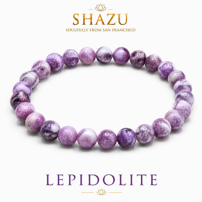 May include: A circular beaded bracelet composed of smooth, round, variegated purple and white lepidolite stones. The image includes the text SHAZU SOULFULLY FROM SAN FRANCISCO at the top and the word LEPIDOLITE in purple text at the bottom.
