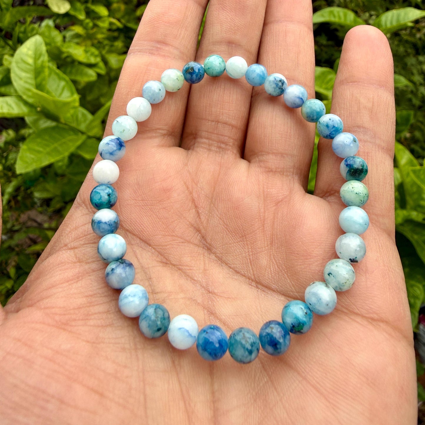 May include: A circular beaded bracelet featuring smooth, polished spherical stones in varying shades of blue, teal, and white. The beads are arranged in a continuous loop, showcasing a marbled texture with translucent and opaque color variations.