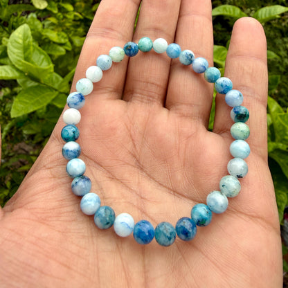 May include: A circular beaded bracelet featuring smooth, polished spherical stones in varying shades of blue, teal, and white. The beads are arranged in a continuous loop, showcasing a marbled texture with translucent and opaque color variations.