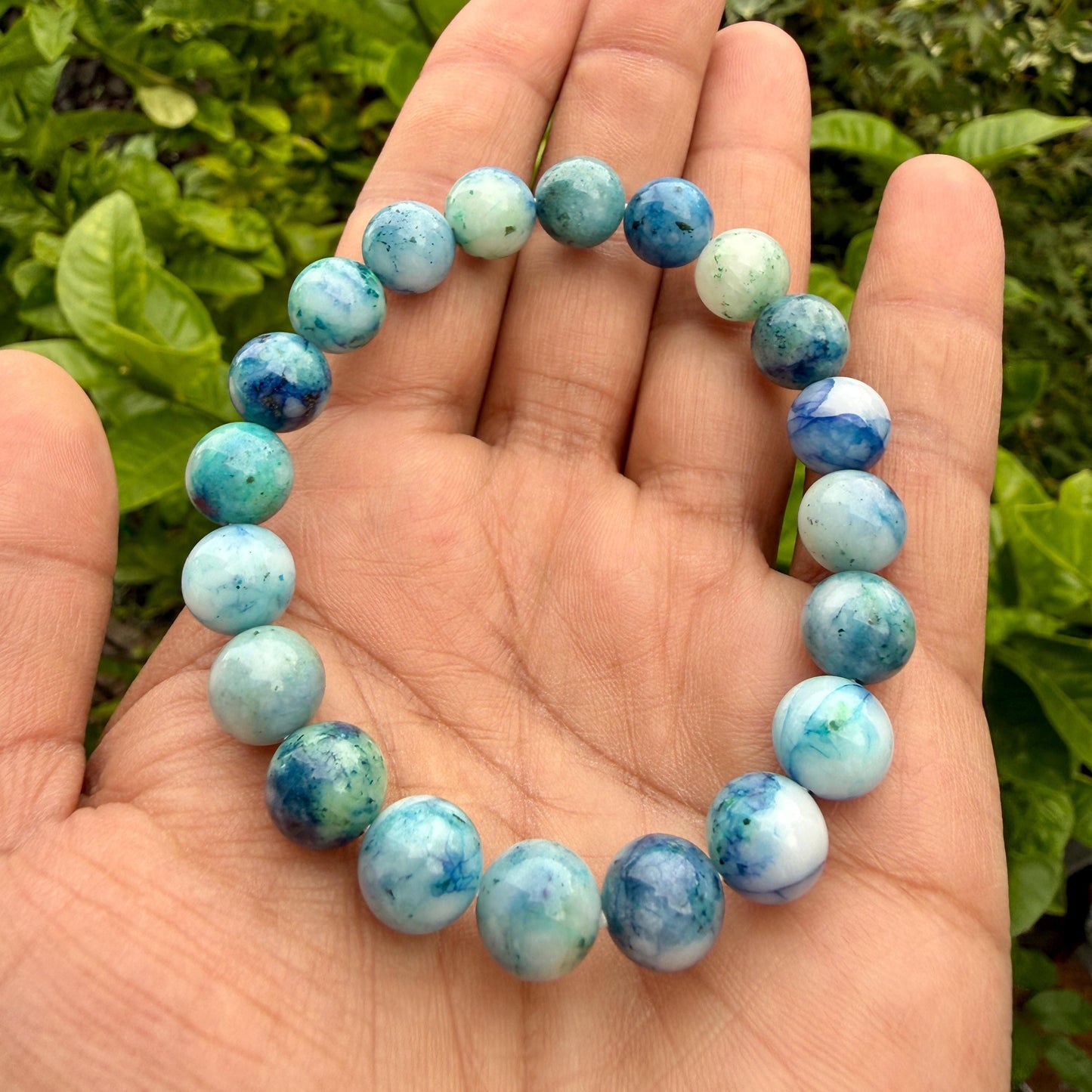 May include: A stretch bracelet composed of round, polished beads in varying shades of blue, teal, and white. The beads feature marbled patterns with translucent and opaque sections, arranged in a circular loop on an elastic cord for easy wear.