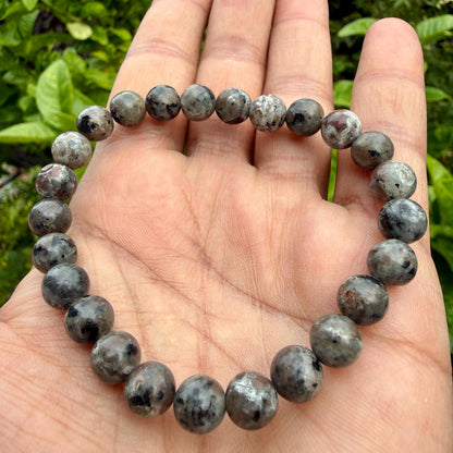 May include: A circular beaded bracelet composed of smooth, round, polished stones in shades of grey, charcoal, and muted brown with speckled, mottled patterns throughout each individual bead, strung together on a flexible, elastic cord.