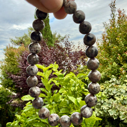 May include: A circular beaded bracelet composed of smooth, polished spherical stones in shades of dark gray, brown, and mottled white. The beads are uniform in size and strung together to form a continuous loop, displaying natural mineral patterns.