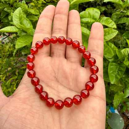 May include: A circular bracelet composed of numerous smooth, translucent, deep red spherical beads strung together. The beads exhibit a consistent glossy finish and a uniform round shape, creating a continuous loop of vibrant red gemstone-like spheres.